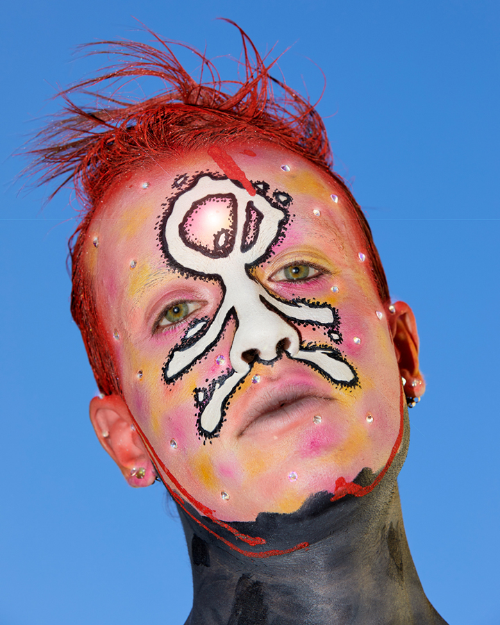 Jesse Clark posing with red and white graphic facepaint on against a sky blue background.